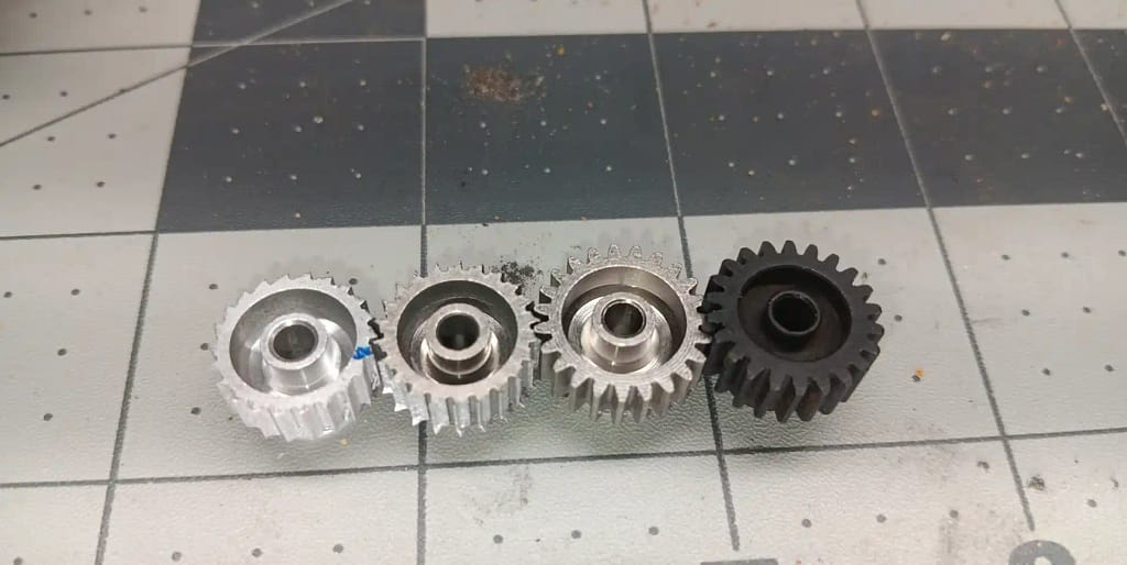 Two worn 22T aluminum pinions compared with a new 23T aluminum pinion and new steel pinion, all Mod 0.6