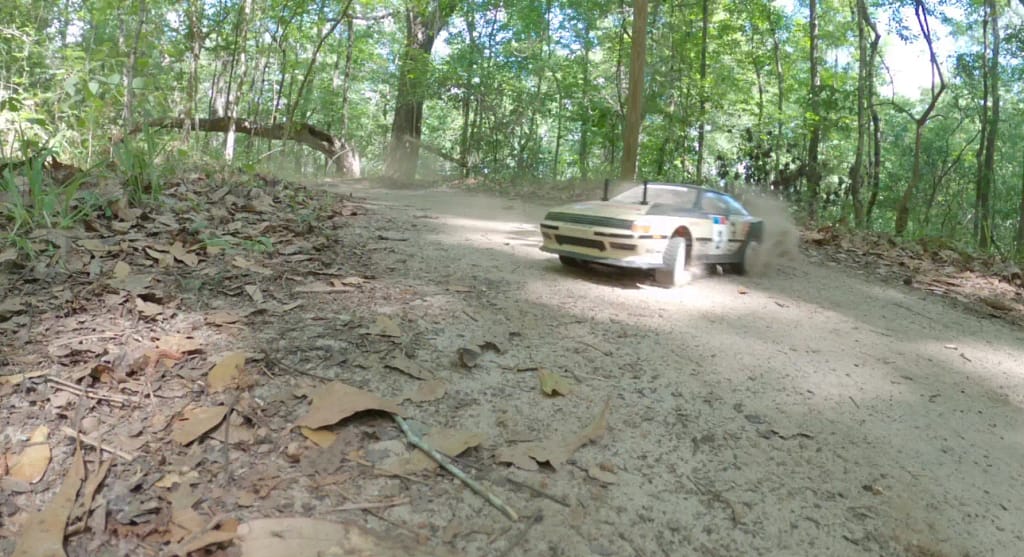 Tamiya TT-02 Celica ST165 rally car sliding around a turn on a dirt bike trail