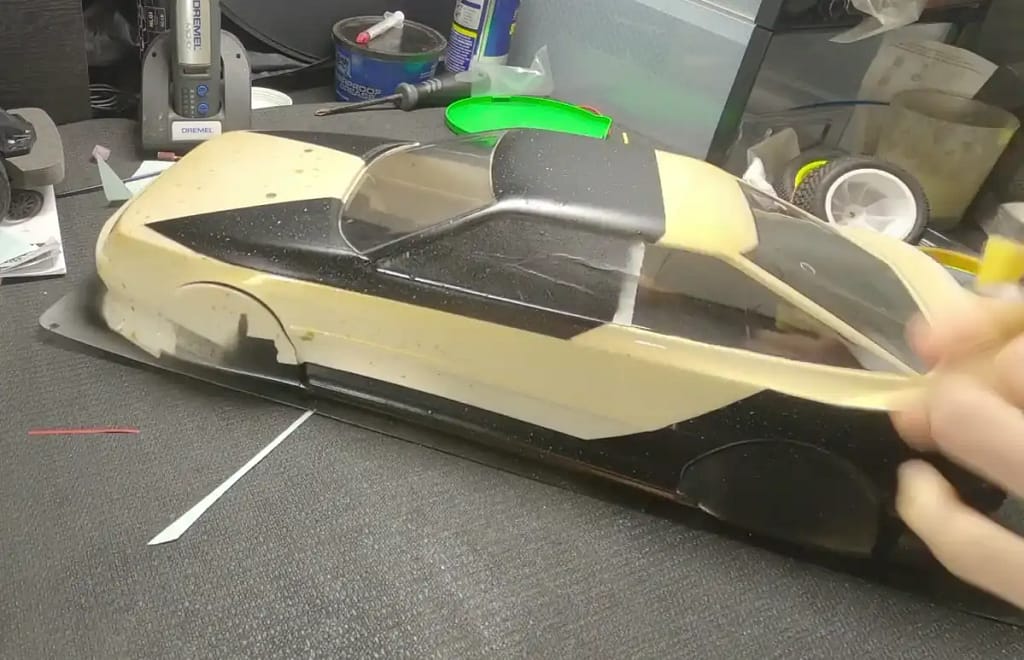 Peeling masking tape from a custom-painted Tamiya TT-02 Celica ST165 body with a black and gold paint scheme