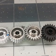 Two worn 22T aluminum pinions compared with a new 23T aluminum pinion and new steel pinion, all Mod 0.6