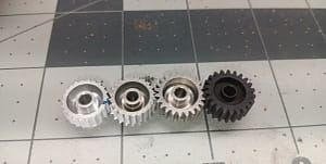 Two worn 22T aluminum pinions compared with a new 23T aluminum pinion and new steel pinion, all Mod 0.6