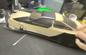 Peeling masking tape from a custom-painted Tamiya TT-02 Celica ST165 body with a black and gold paint scheme